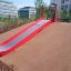 Hill Slide Wide SLW180 red and grey playground slide on a sloped hill in an urban park