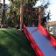 Hill Slide Wide SLW180, red and silver slide on artificial grass hill in a playground.
