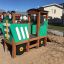 Green Tractor-themed playground structure in a sandy play area.