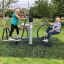 Two seniors using outdoor gym equipment Set 8 on a grassy park area.