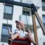 Young girl smiling and swinging on a red swing attached to Double Swing with Tower playhouse with sl