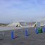 Skate park ramps and rails with blue bollards and green trash cans.