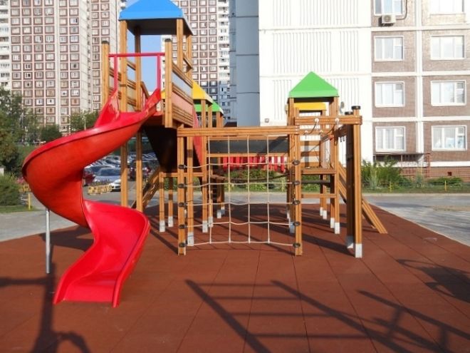 Children's playground with wooden structures and red slide on Rubber Tiles 75.