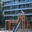 Explorer wooden playground with slide and climbing elements on a sandy surface in front of modern re