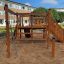 Wooden playhouse with slide, climbing ladder, and sandbox.