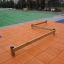 Balance beam playground equipment on an orange mat with a green field in the background.
