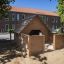 Veranda House Nature wooden playhouse in a sandbox with trees and building in the background