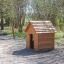 Wooden Nature Playhouse in a park setting with a swing in the background.