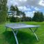 Outdoor Table Tennis in a grassy outdoor setting with trees in the background.
