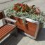 Oxford Flowerpot made of wood and metal, filled with red flowers and green plants, placed next to a 
