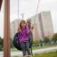 Child playing on a Single swing tire seat in a playground with high-rise buildings in the background