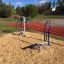 Outdoor gym equipment set placed on woodchip ground near a running track.
